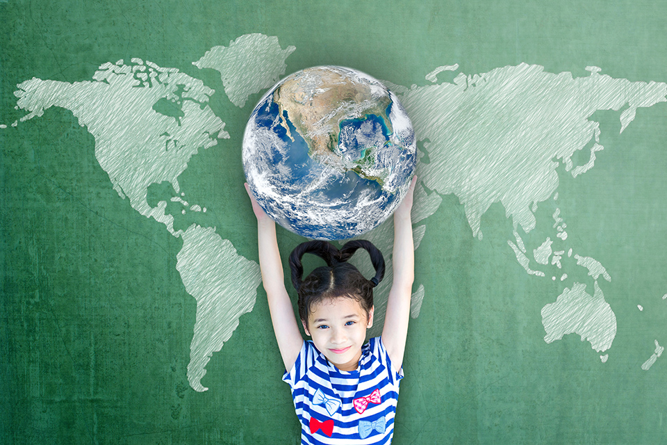 A photo of a girl holding up a globe of the world in front of a map for the Grade 5 Natural Sciences Planet Earth and Beyond topic.